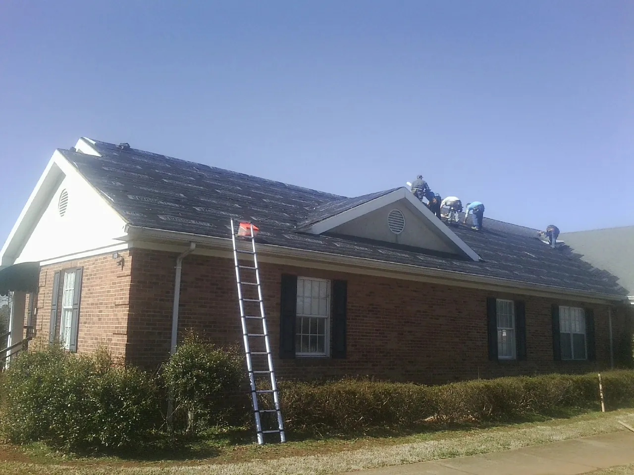 Crew tearing shingles off a brick ranch roof with a ladder set — Emergency Roof Repair work by our crew in Nitro