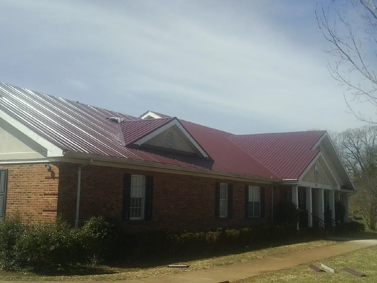 Red metal roof with gabled entries on a long brick building, from a Hail Damage Roof Repair job in Nitro