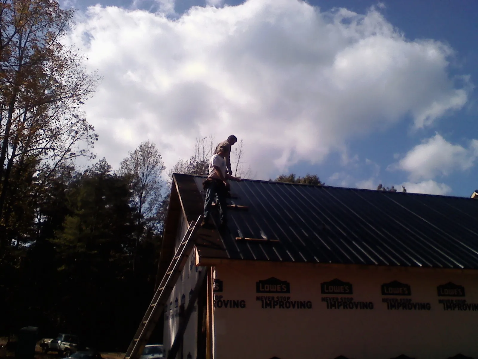 Roofer fastening dark metal panels high against a cloudy sky, from a Roof Inspection job in Nitro